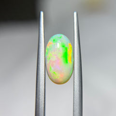 Opal gemstone held between tweezers against a blurred background